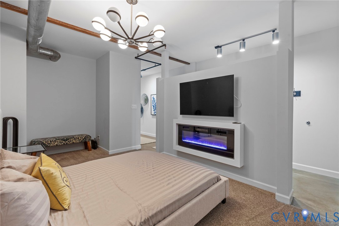 Space featuring a wall-mounted electric fireplace, exposed industrial ductwork, a multi-arm statement chandelier, and adjustable track lighting