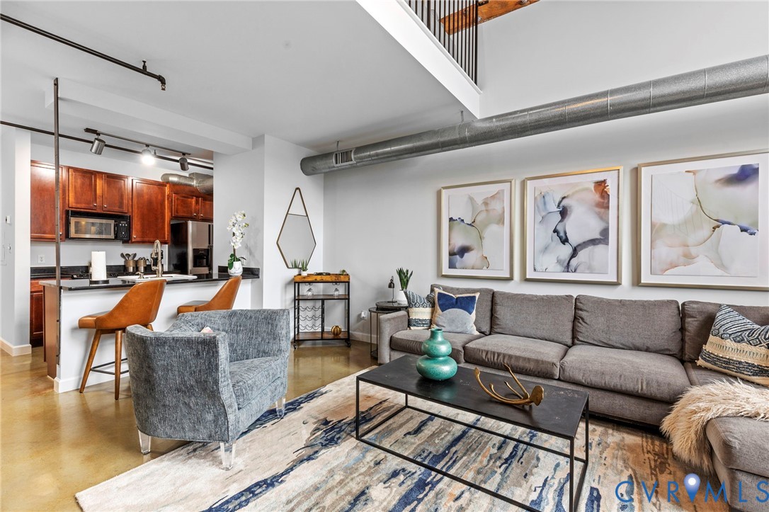 Open-concept interior featuring high ceilings, exposed ductwork, polished concrete flooring, kitchen with built-in cabinetry, and integrated track lighting