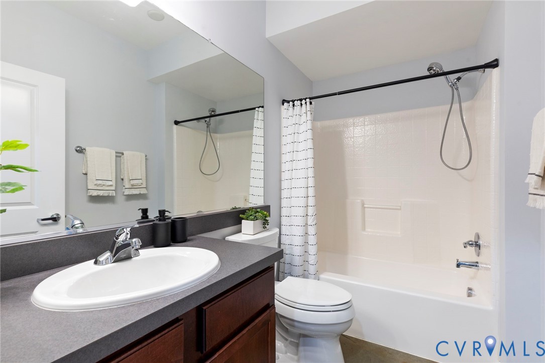 Full-width vanity with a dark countertop and integrated sink, complemented by a large wall-mounted mirror, wood-finish cabinetry, and a shower-tub combination with a handheld fixture