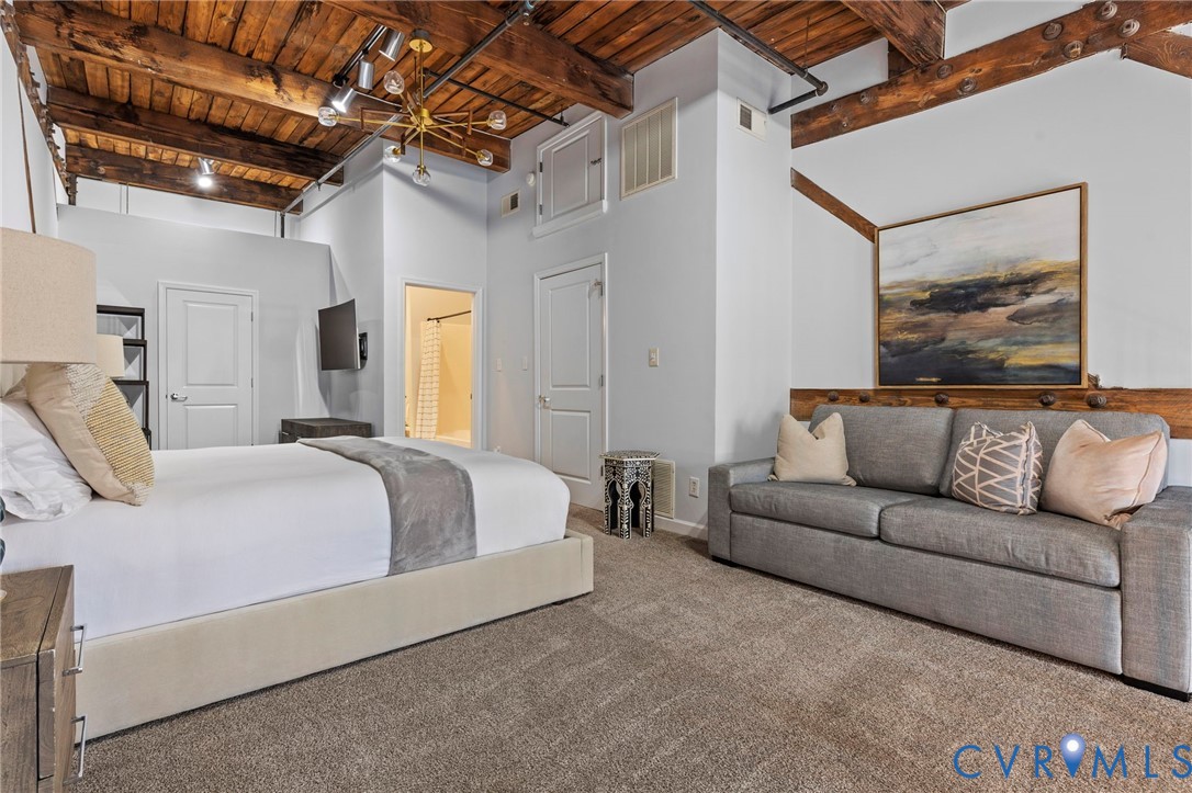 Exposed timber ceiling beams, industrial-style pipe conduit, multi-arm metal chandelier, and neutral wall-to-wall carpeting