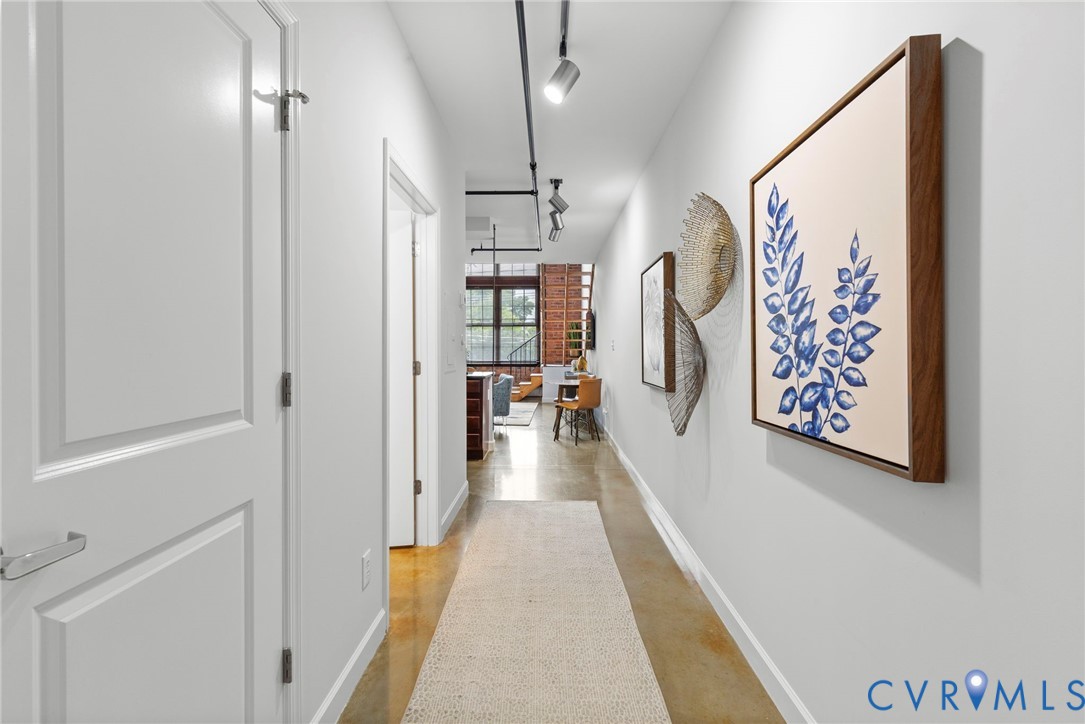 Industrial-style hallway featuring polished concrete flooring, exposed overhead track lighting, and exposed brick structural elements