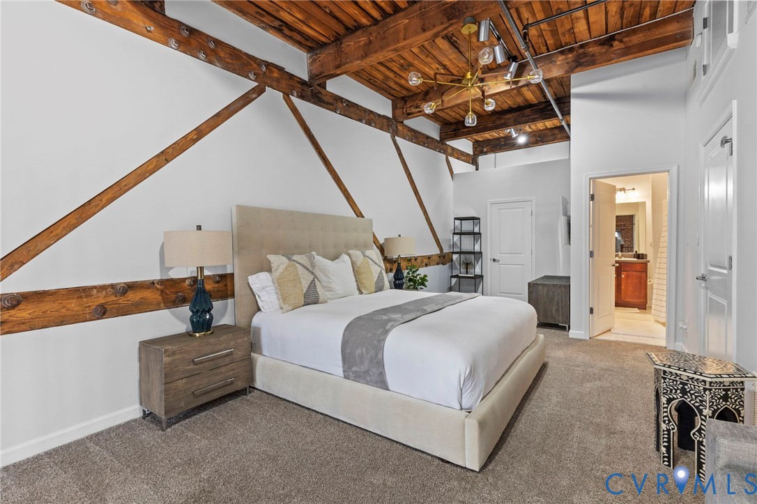 Exposed wood ceiling beams, decorative structural wall bracing, high ceilings, brass-finish chandelier, and neutral wall-to-wall carpeting