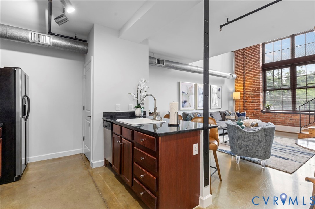 Industrial-style loft featuring exposed brick walls, expansive multi-pane windows, polished concrete flooring, open-concept kitchen with dark stone countertops, and overhead structural steel support