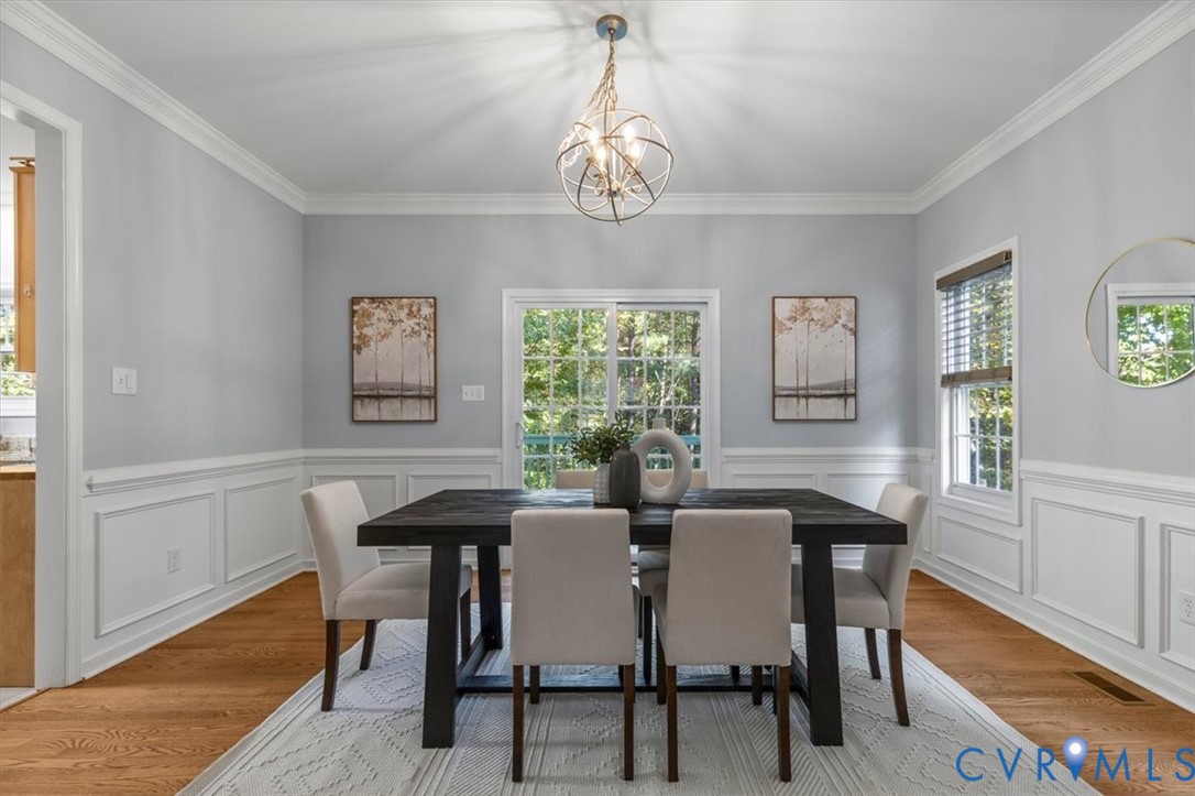 Dining area featuring wood flooring, crown molding, decorative wainscoting, sliding glass doors, and chandelier