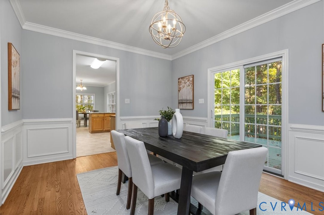 Dining area featuring wood flooring, crown molding, decorative wainscoting, sliding glass doors, and chandelier