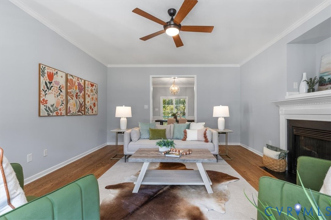 Living area featuring wood flooring, a fireplace, crown molding, and ceiling fan