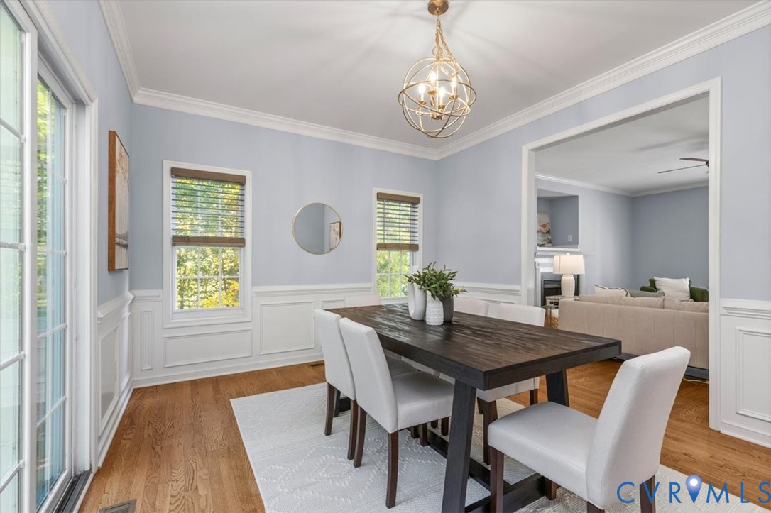 Dining area featuring wood flooring, crown molding, decorative wainscoting, sliding glass doors, and chandelier