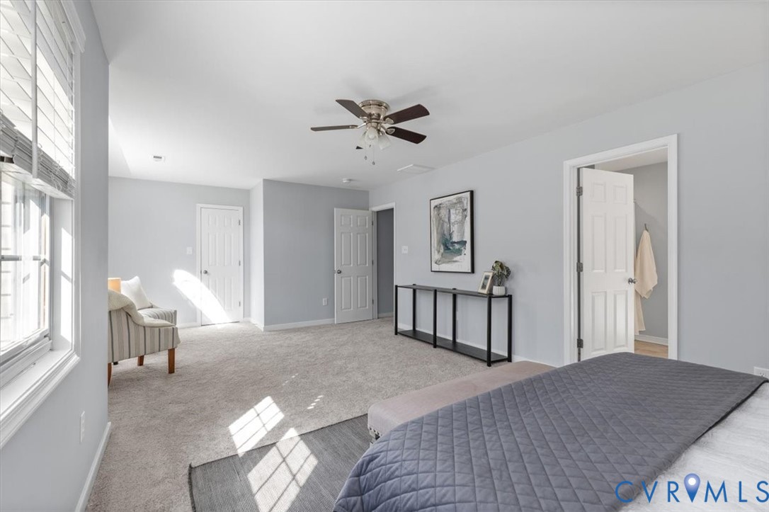 Primary bedroom featuring ensuite, new carpeting, ceiling fan, sitting area, and huge walk in closet