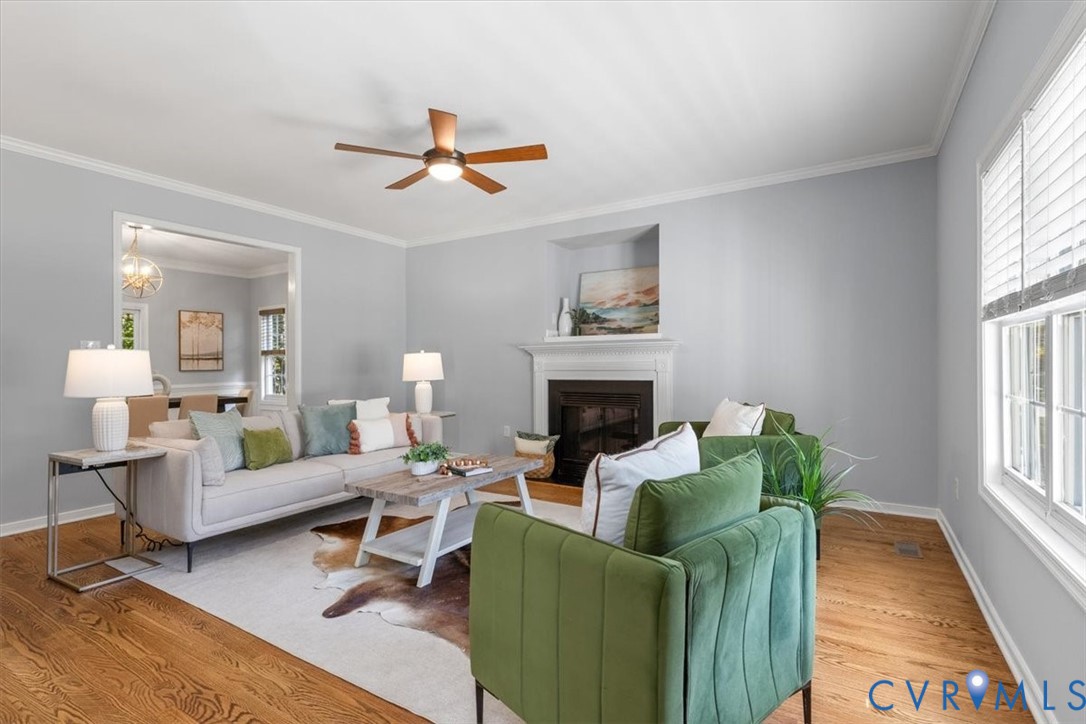 Living area featuring wood flooring, a fireplace, crown molding, and ceiling fan