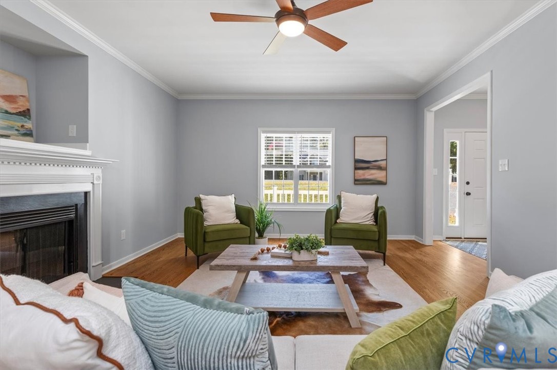 Living area featuring wood flooring, a fireplace, crown molding, and ceiling fan
