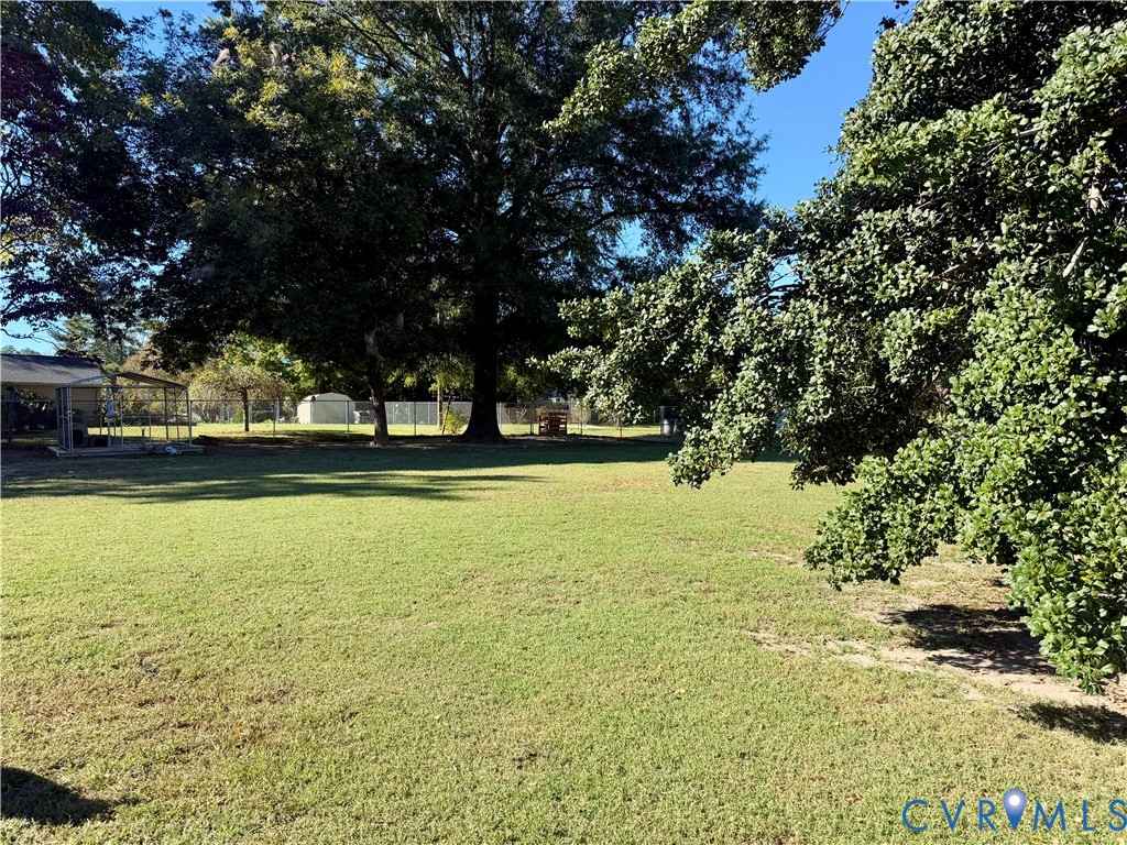 Expansive backyard featuring a large grass lawn, mature trees, a metal-framed structure, and perimeter fencing