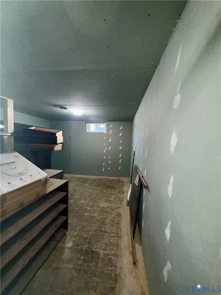 Unfinished space featuring gypsum board wall panels, a ceiling-mounted light fixture, and a rectangular egress window