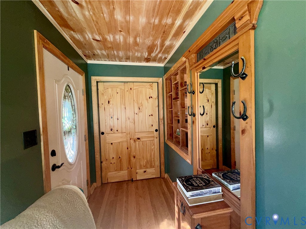 Entryway featuring a wood-planked ceiling, natural wood-finished interior doors, built-in shelving, and a decorative wall-mounted mirror with integrated iron hooks
