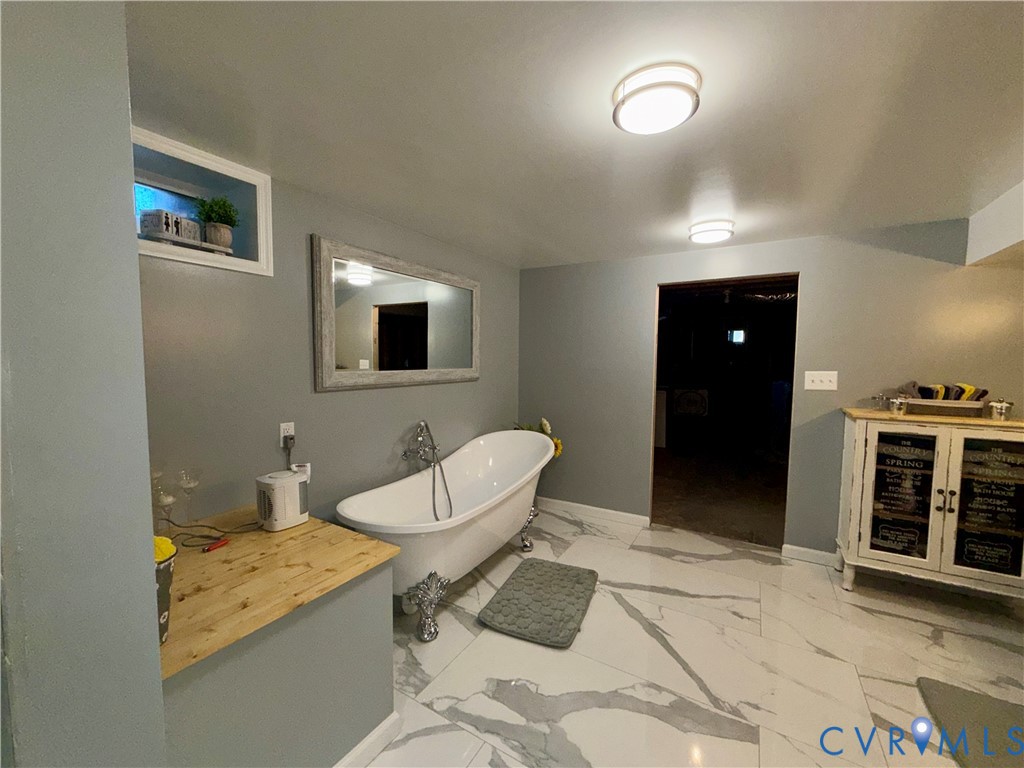 Freestanding clawfoot tub with chrome telephone-style faucet, large-format stone-patterned tile flooring, recessed wall niche, and flush-mount ceiling lighting