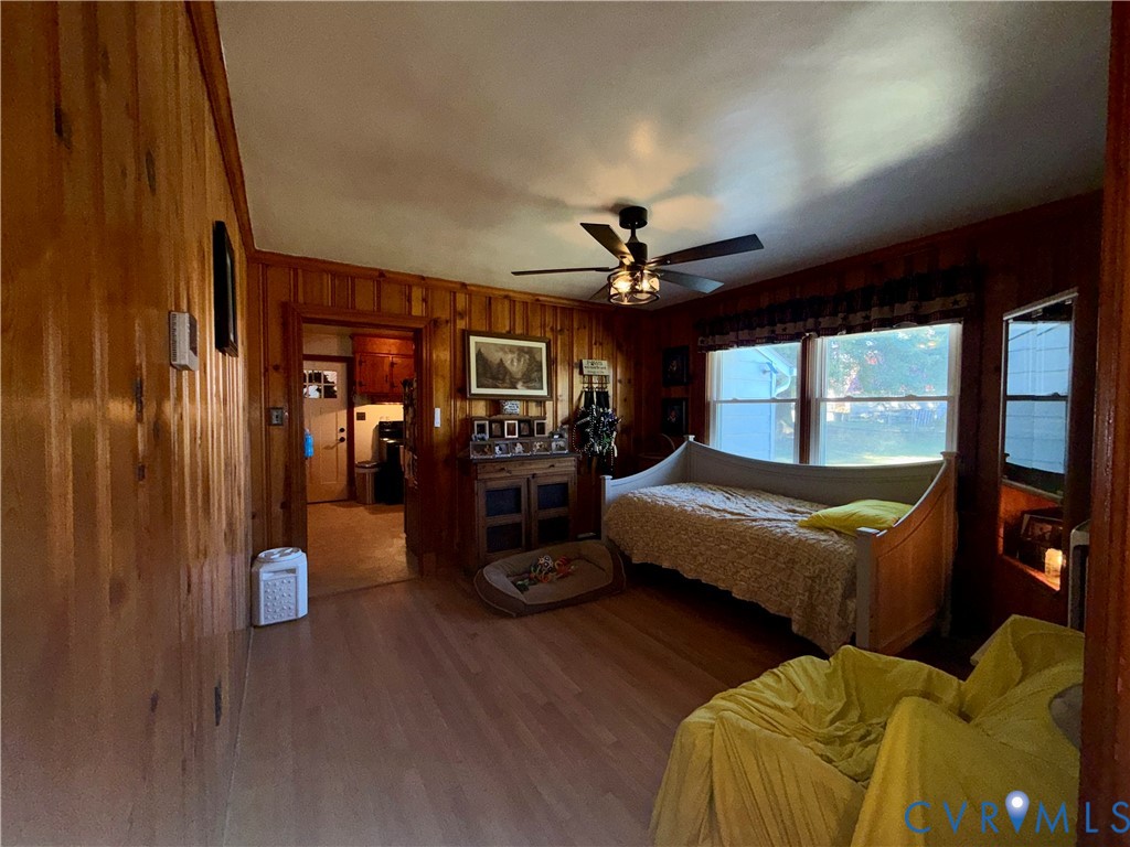 Wood-paneled walls, light-toned wood-finish flooring, and a ceiling fan with integrated lighting