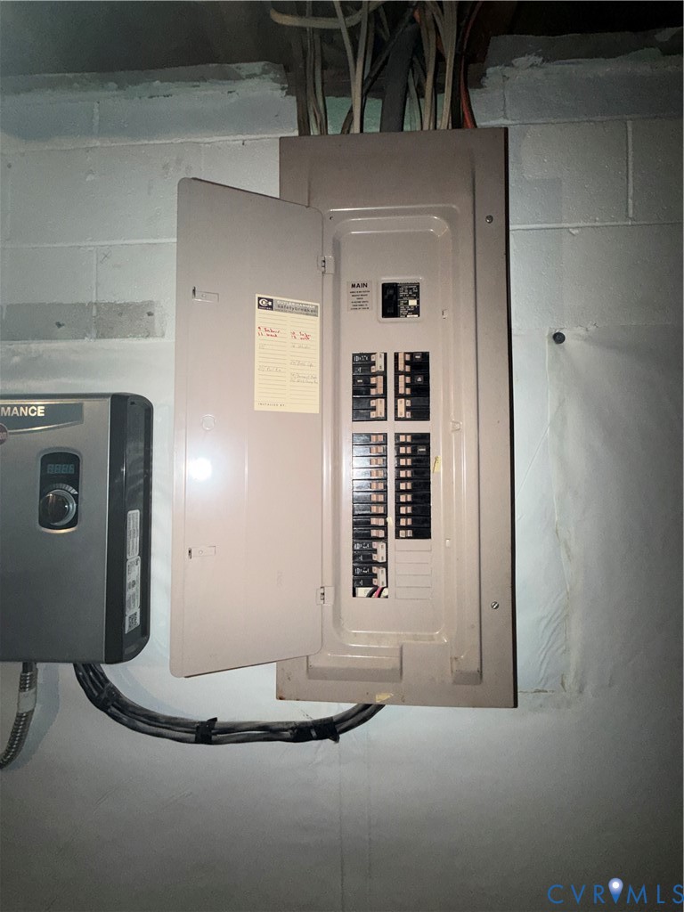 Electrical service panel featuring a main breaker and a multi-circuit configuration, mounted on a concrete block wall alongside a wall-mounted electronic control unit