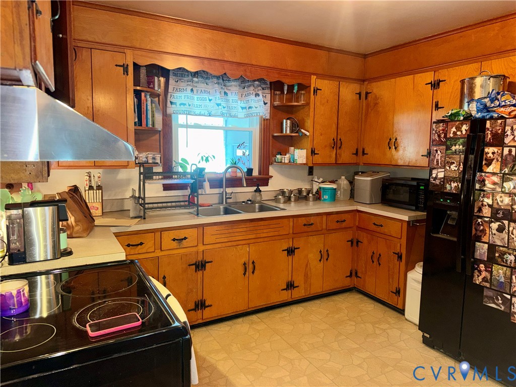 Kitchen featuring extensive wood cabinetry, solid-surface countertops, dual-basin stainless steel sink, and stainless steel range hood
