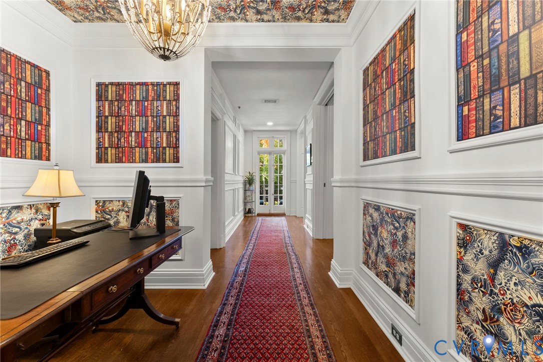 Hardwood flooring, decorative wall paneling with patterned inlays, ceiling-mounted metal chandelier, and double glass-paned doors