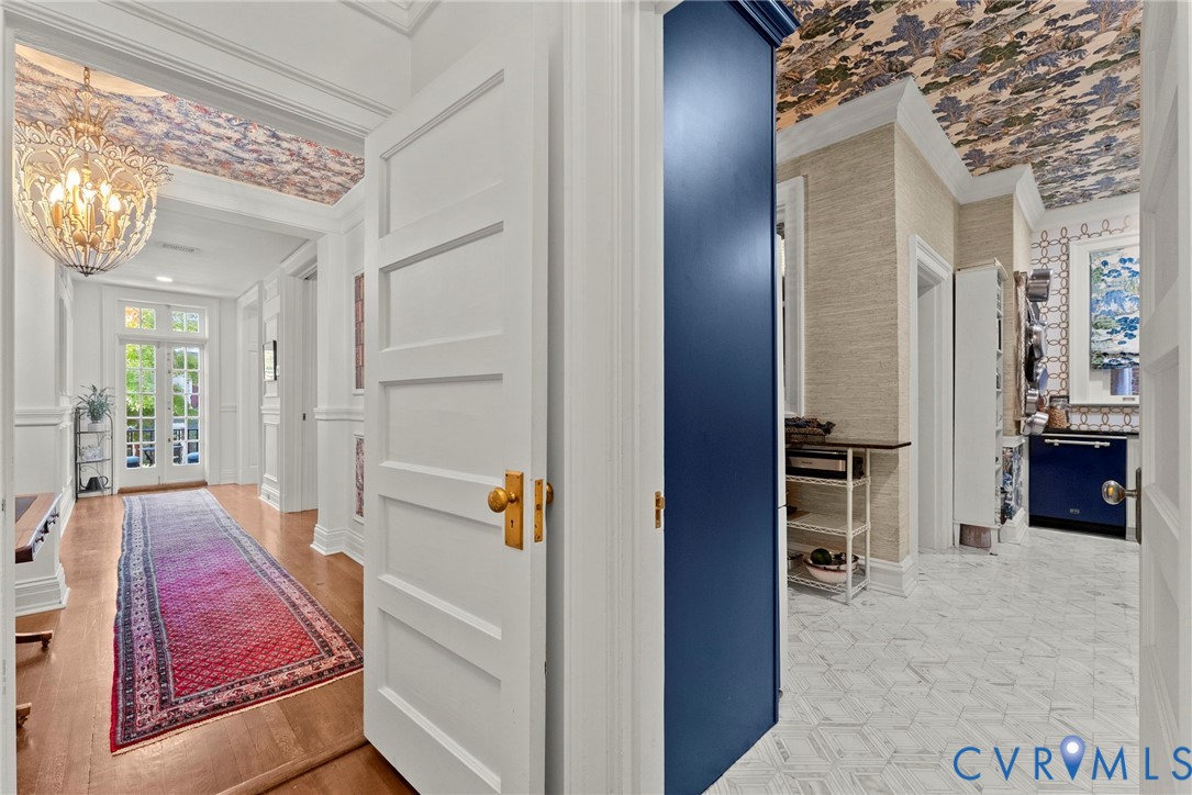 Entryway featuring wood-finish flooring, ornate multi-arm chandelier, and decorative wallpapered ceiling