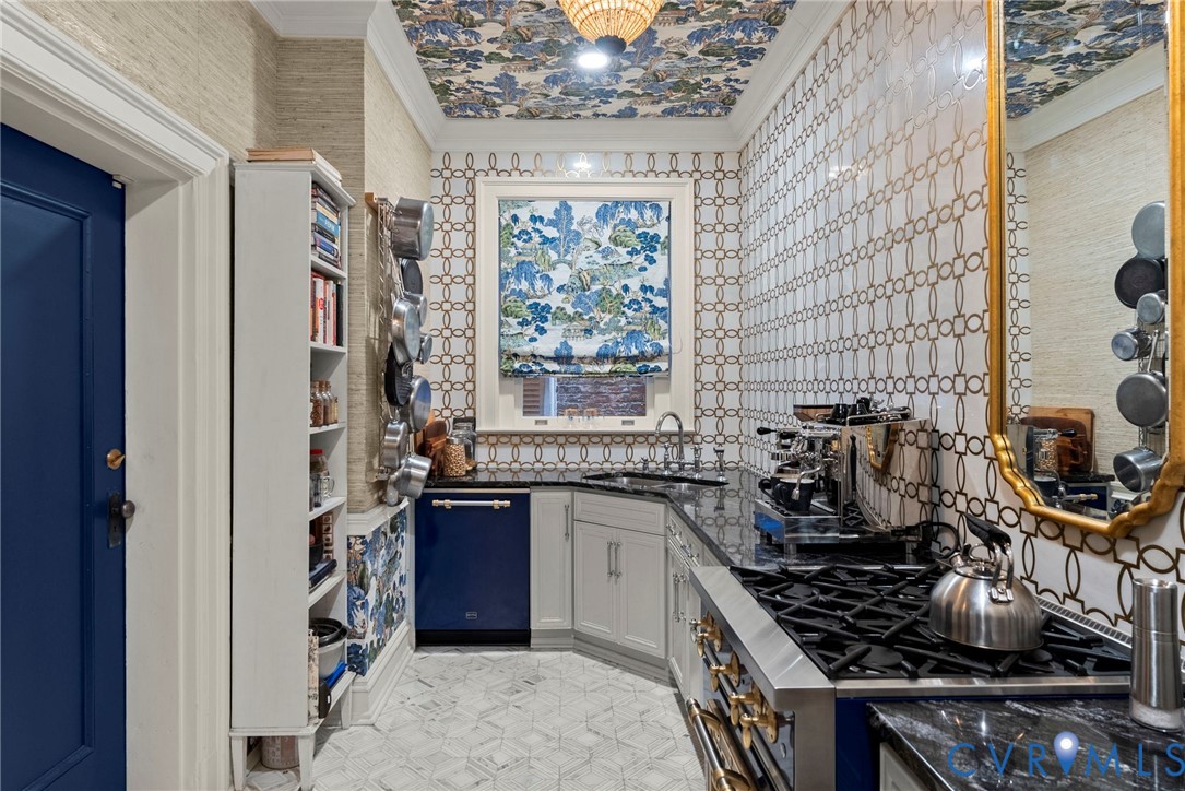 Kitchen featuring patterned tile walls, geometric stone flooring, integrated blue dishwasher, stainless steel gas range, and built-in shelving