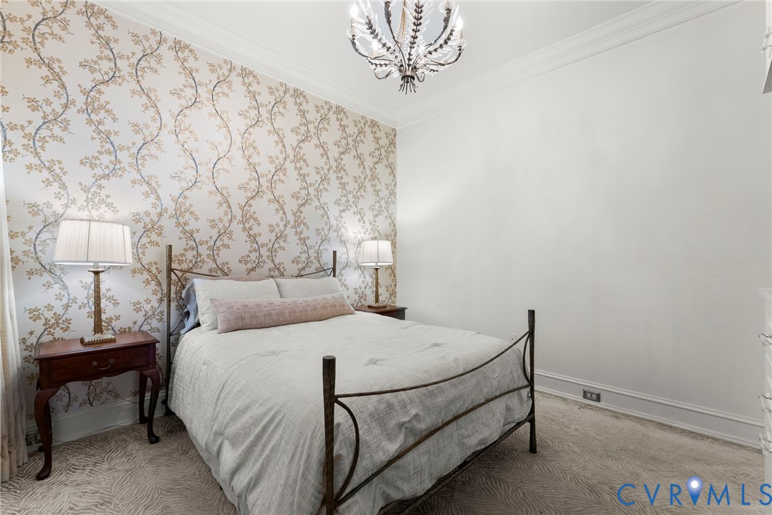 Room featuring an accent wall with floral patterned wallpaper, crown molding, and a decorative multi-arm chandelier