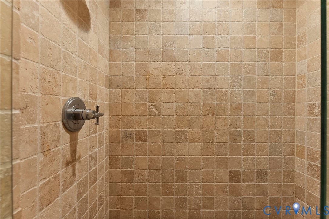 Shower enclosure featuring floor-to-ceiling square stone-finish tiles and a brushed metallic cross-handle pressure balance valve