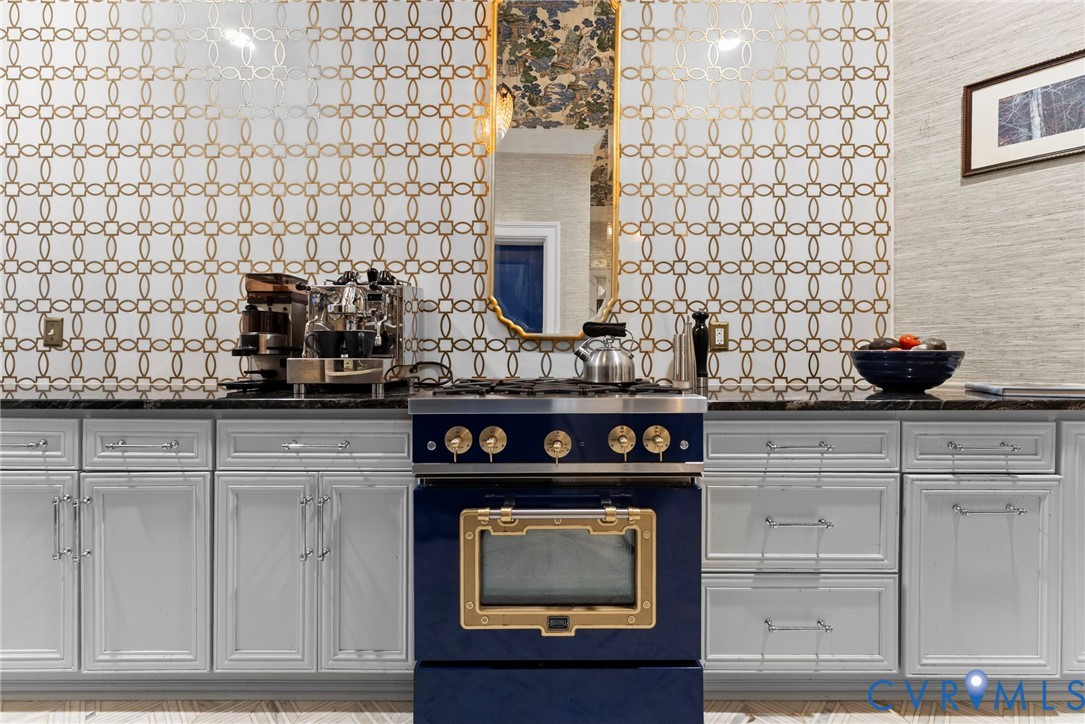 Custom cabinetry with shaker-style doors, metallic geometric wall tile, stone countertop, and navy blue range with gold-tone hardware
