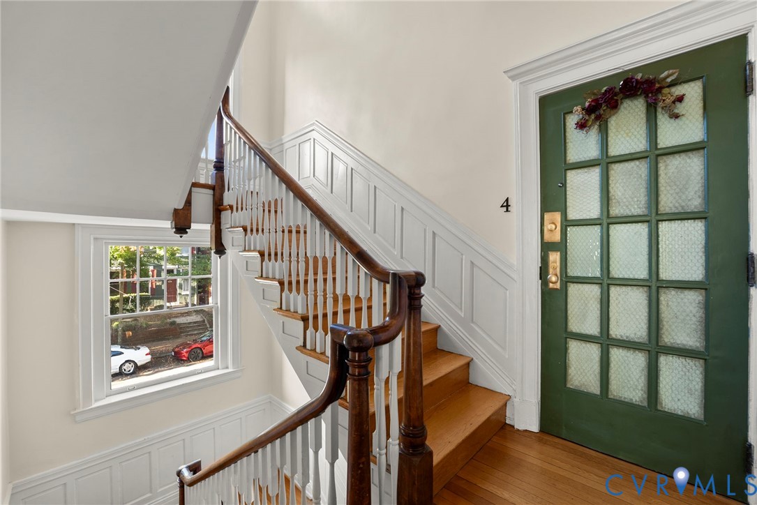 Entryway featuring a green-painted paneled door with glass inserts, wood-finish staircase with a turned wooden banister, wall paneling, and wood-finish flooring