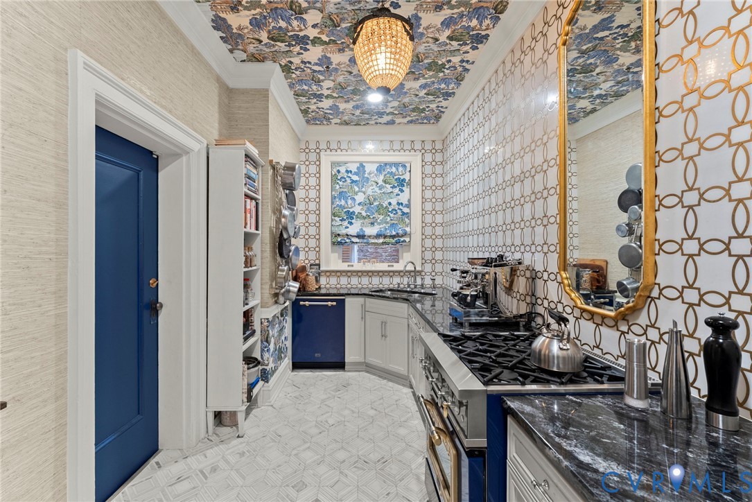 Kitchen featuring stone countertops, geometric patterned tile walls, built-in cabinetry, an integrated dishwasher, and a crystal chandelier fixture