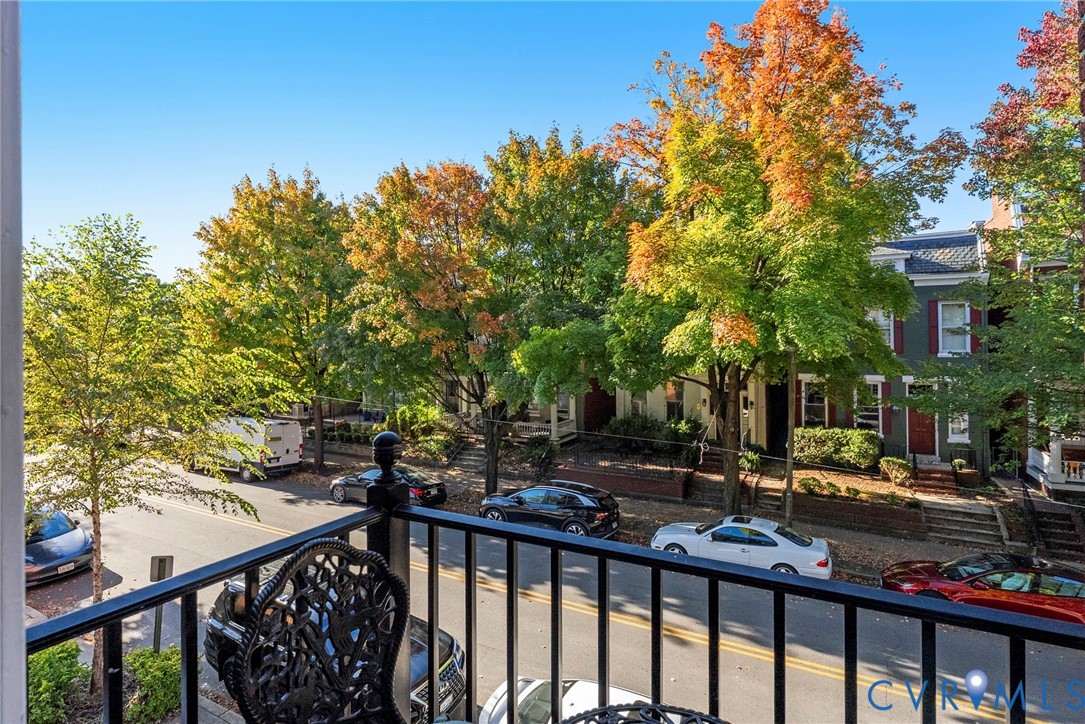 Elevated exterior balcony featuring black metal railings and mature trees