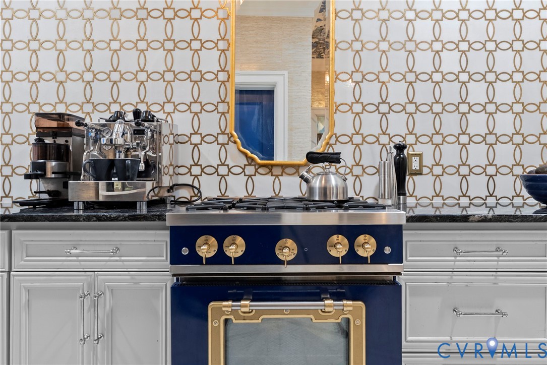 Custom cabinetry with silver-tone hardware, dark stone-finish countertops, geometric-patterned wall tile, and a professional-grade blue and gold-tone gas range