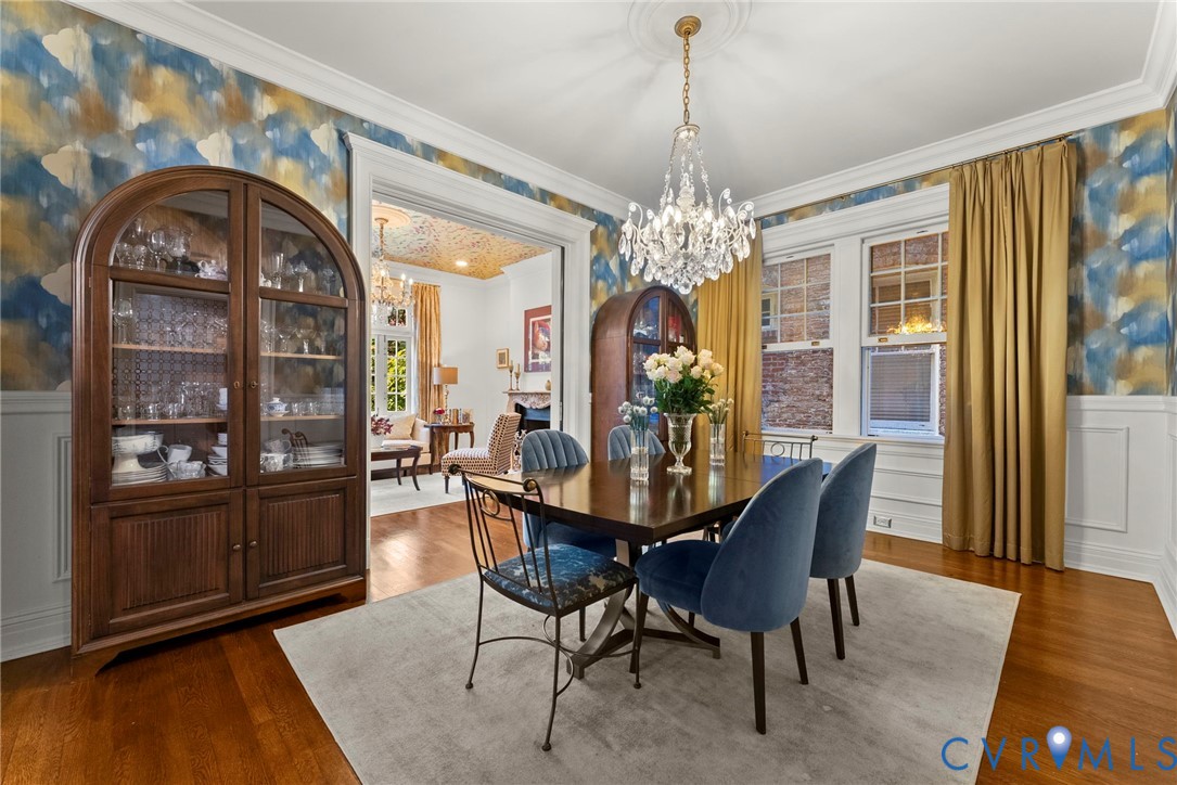 Dining space featuring decorative wainscoting, intricate ceiling medallion, crystal chandelier, and hardwood flooring