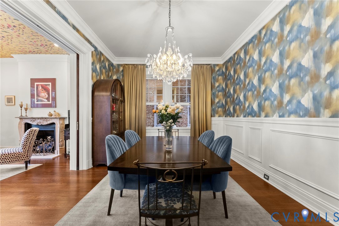 Dining room featuring intricate crown molding, extensive wainscoting, a crystal chandelier, wood-finish flooring, and a decorative fireplace with carved mantle