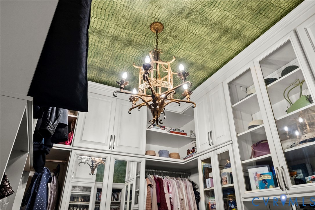Custom built-in cabinetry with glass-front display doors, metallic hardware, integrated hanging rods, and a decorative pendant fixture finished with a distinctive patterned ceiling treatment