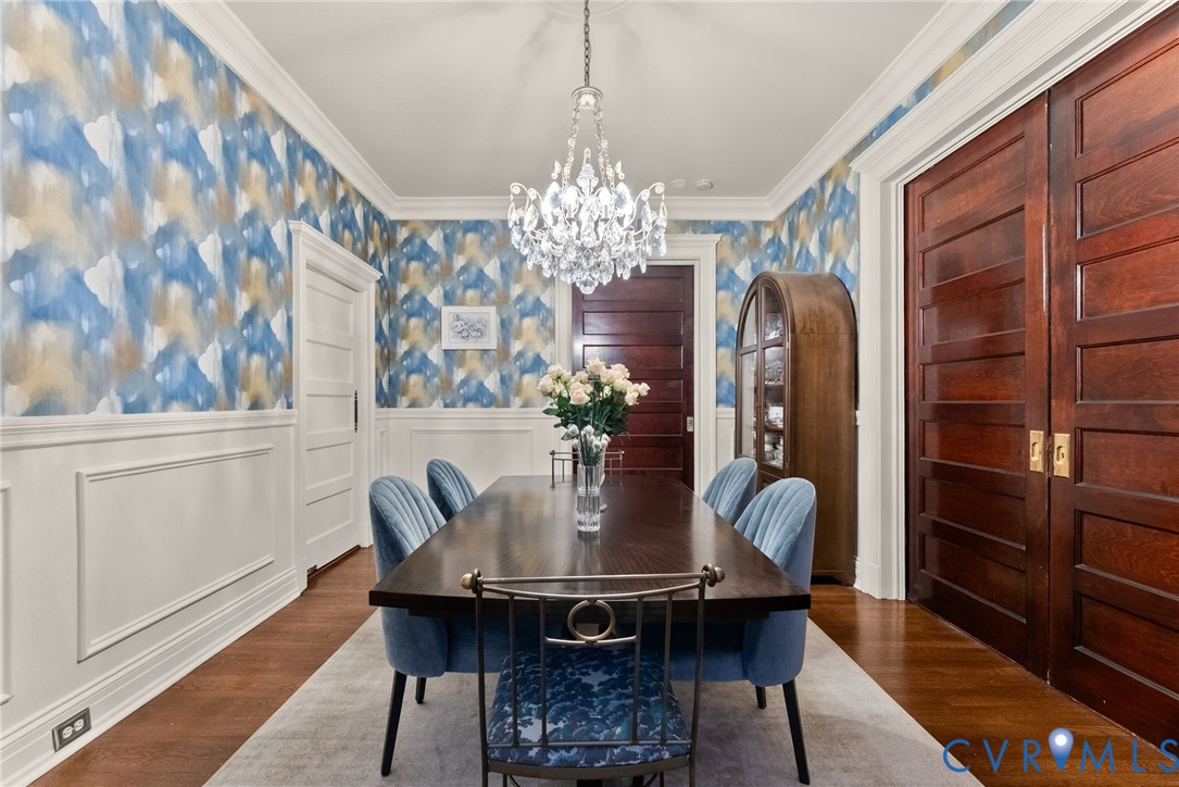 Dining space featuring stained wood flooring, custom wainscoting, solid wood doors, and a crystal chandelier