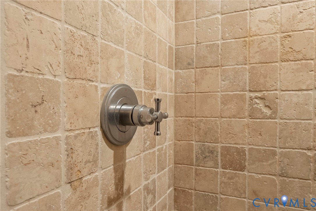 Shower surround featuring square-cut natural stone tile and a metallic single-handle control valve