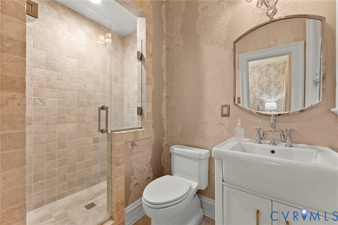 Walk-in shower with natural stone tiling and glass enclosure, porcelain pedestal sink with polished metal bridge faucet, and ornate wall-mounted mirror