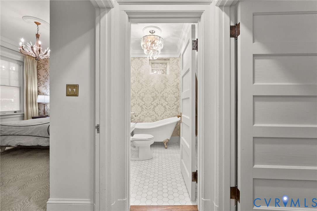 Bathroom featuring a clawfoot soaking tub, patterned wallpaper, crystal-style chandelier, and white hexagonal tile flooring