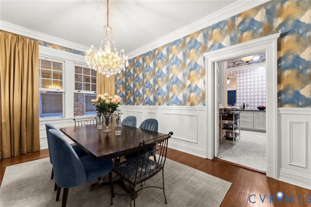 Dining area featuring decorative wall covering, wainscoting, hardwood flooring, crown molding, and a multi-arm crystal chandelier