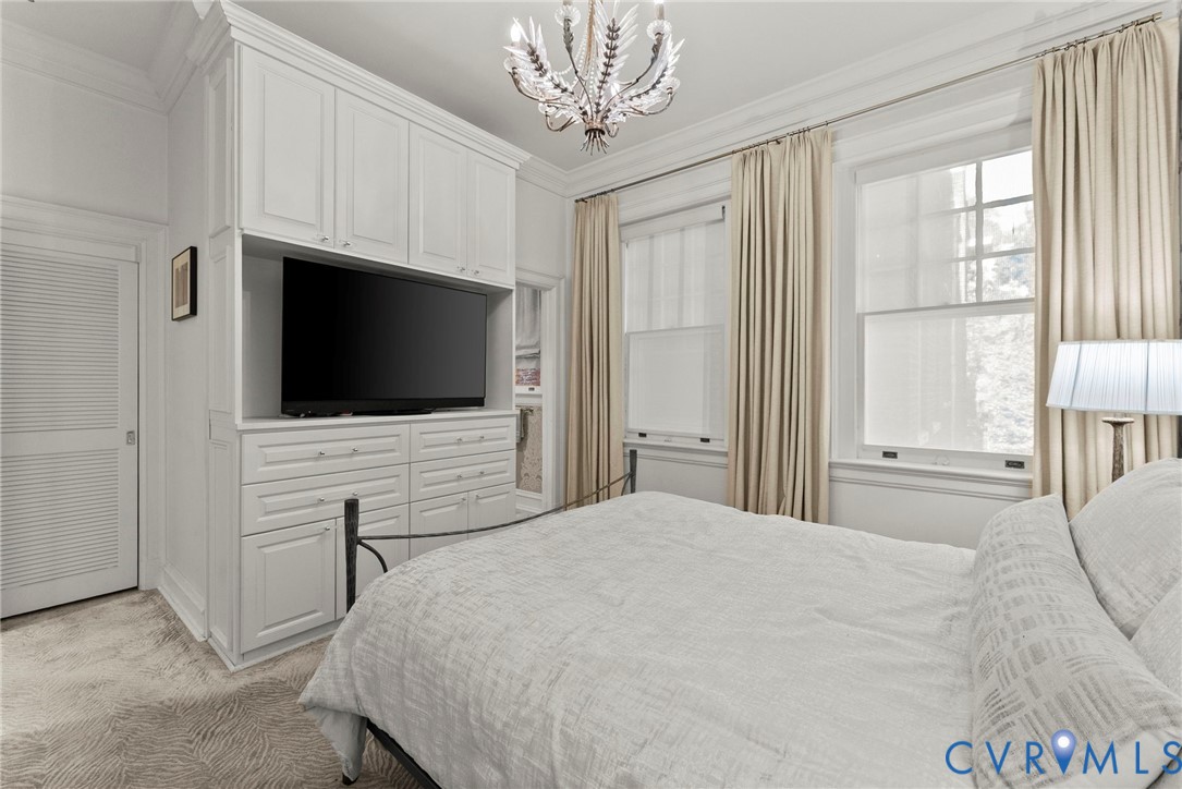Custom floor-to-ceiling built-in cabinetry, ornate ceiling chandelier, crown molding, double-hung windows, and louvered door