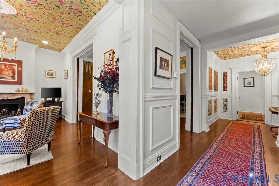 Intricate ceiling wallpaper, ornate crystal chandeliers, wall wainscoting, decorative fireplace mantle, and wood-finish flooring