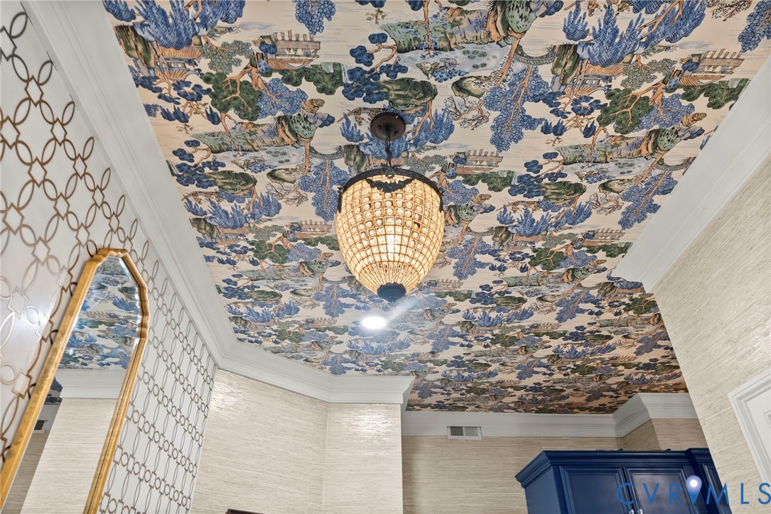 Intricate patterned ceiling wallpaper, multi-tiered beaded chandelier, textured wall coverings, crown molding, and geometric-patterned wall accent
