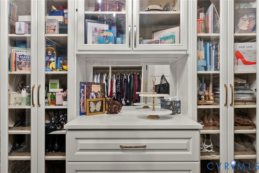 Built-in cabinetry featuring white shaker-style doors, glass-paneled display shelving, integrated vanity surface with mirror, and metallic hardware