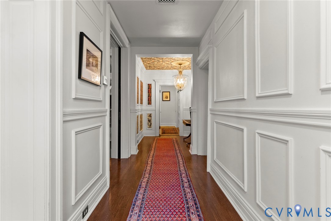 Hallway featuring extensive wainscoting and molding, wood-finish flooring, decorative ceiling pattern, and a central crystal chandelier
