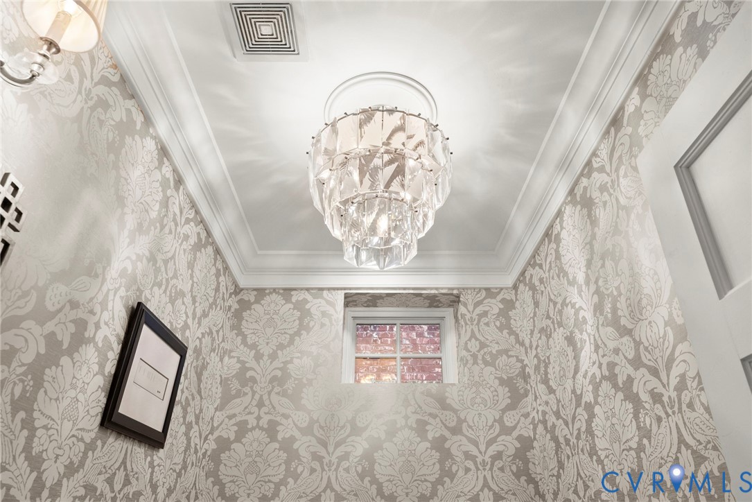 Tiered crystal chandelier with a ceiling medallion, crown molding, and patterned wallpaper