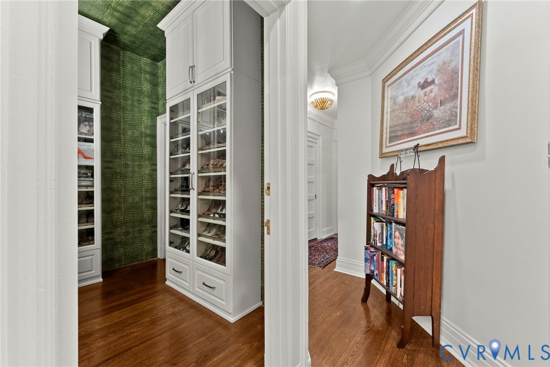 Custom white floor-to-ceiling cabinetry with glass-panel doors, integrated shelving, and dark-toned hardware, featuring wood-finish flooring and patterned wall coverings