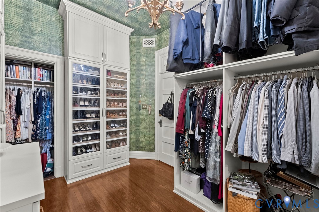 Custom dressing room featuring floor-to-ceiling cabinetry, glass-front shelving, integrated storage drawers, and wood-finish flooring