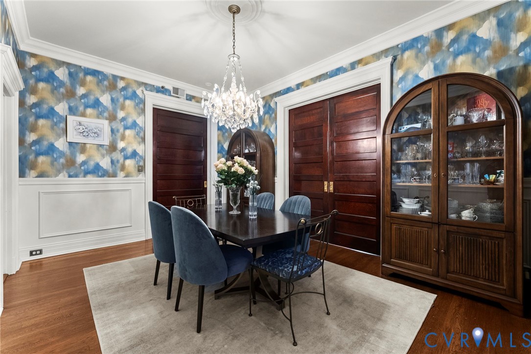 Formal dining area featuring hardwood flooring, wainscoting, crown molding, tiered crystal chandelier, and deep-toned wood doors