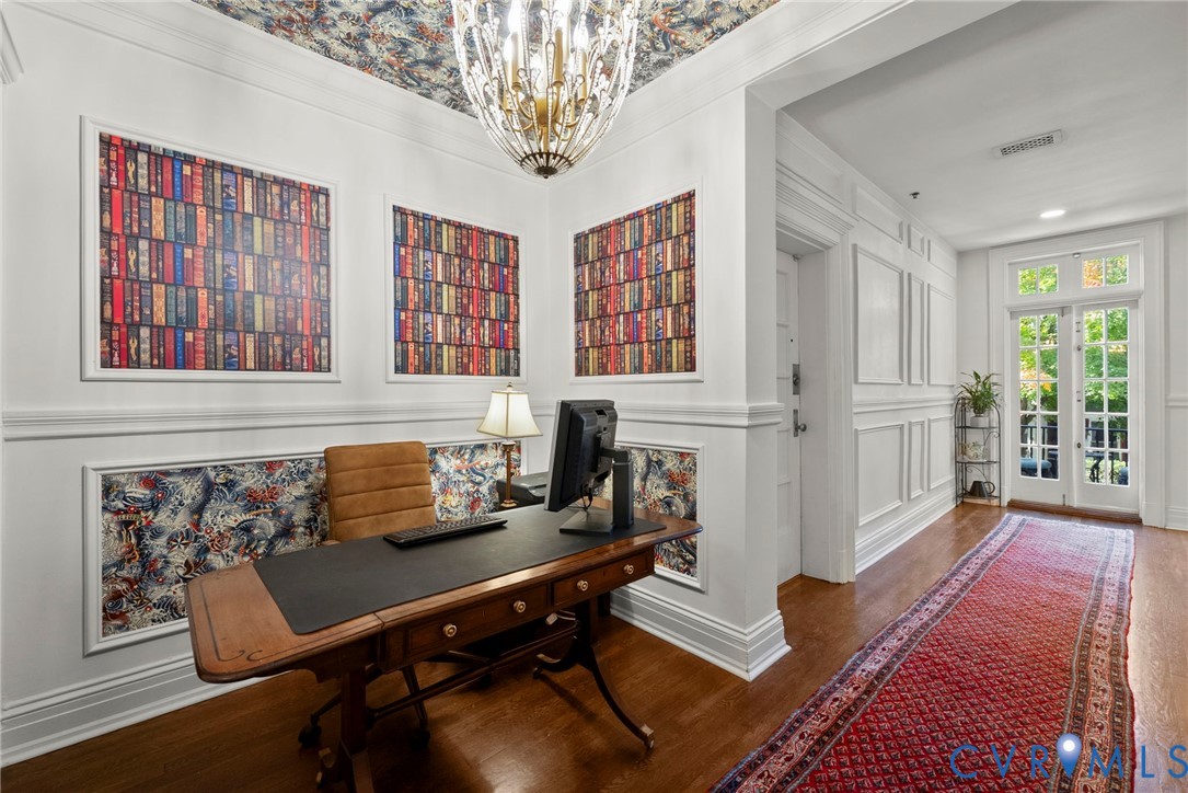 Custom millwork featuring wainscoting and picture frame molding, decorative wallpaper inlay, hardwood flooring, crystal chandelier, and glass-paned French doors