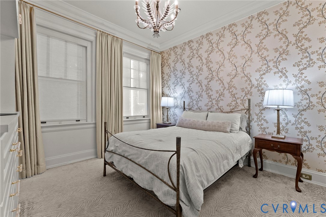 Interior room featuring patterned wallpaper, crown molding, double-hung windows, and a decorative chandelier